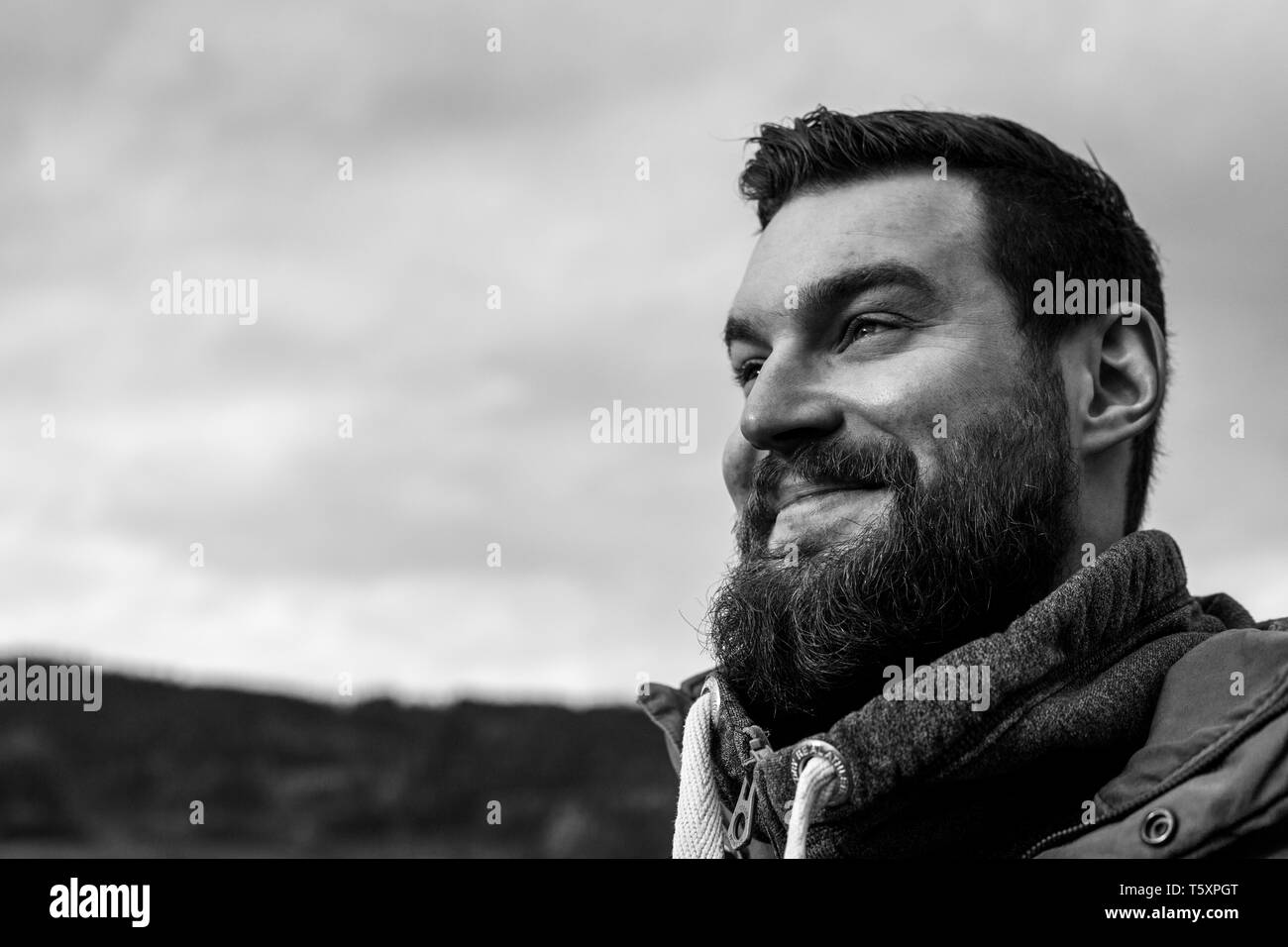 Young attractive bearded man with dark hair and a pullover in the park smiling Stock Photo