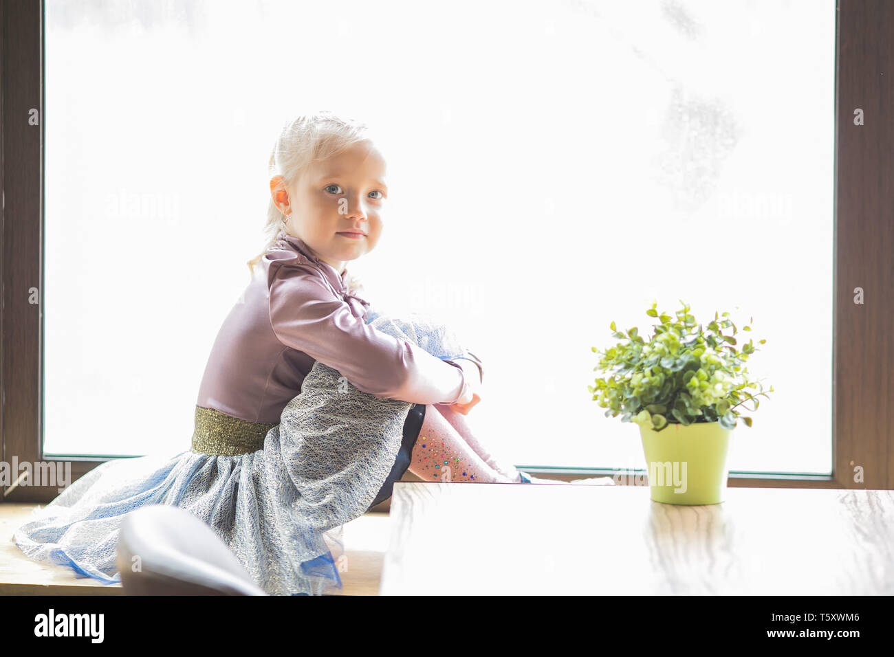 A Little Girl 4 5 Years Old Is Sitting On The Windowsill Of A