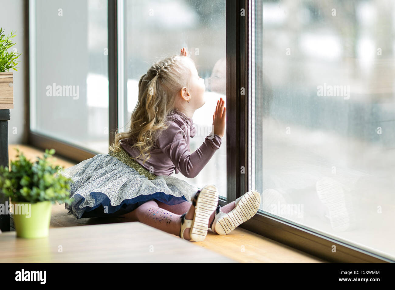 A Little Girl 4 5 Years Old Is Sitting On The Windowsill Of A