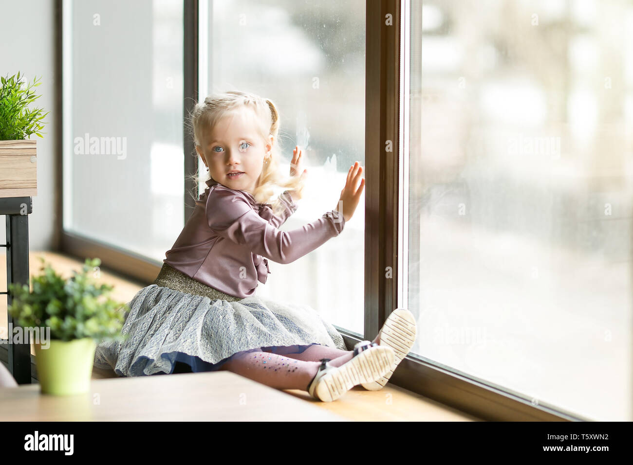 A Little Girl 4 5 Years Old Is Sitting The Windowsill Of A Large
