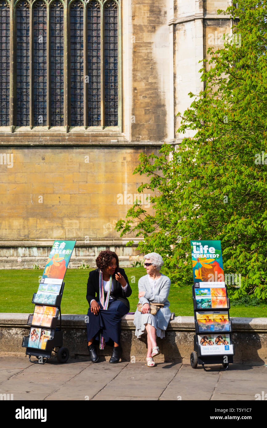 Two Jehovahs Witnesses ladies sitting on the wall of kings College Chapel, with Chinese and English pamphlets. University town of Cambridge, Cambridge Stock Photo