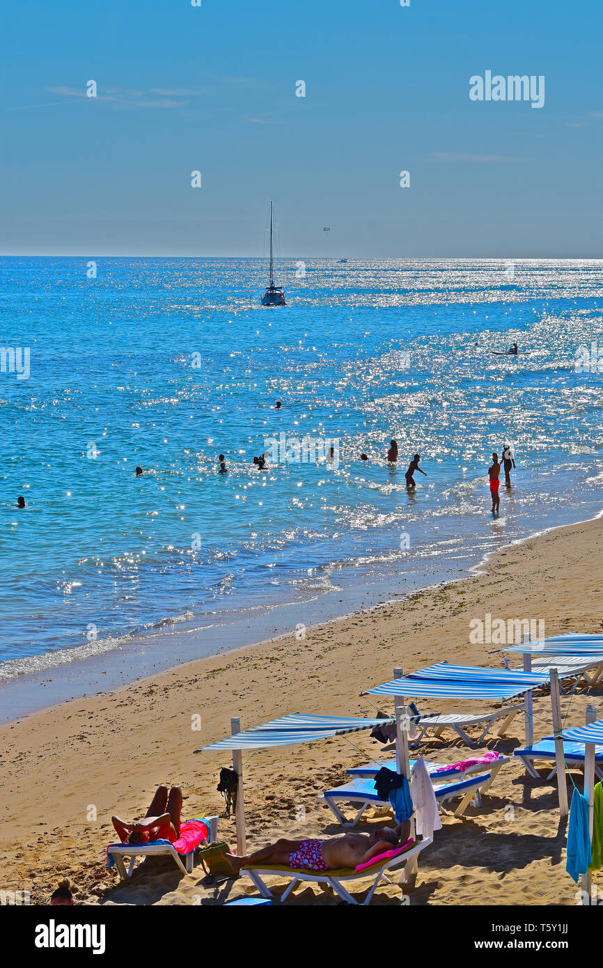 A stunning view of the beach and shimmering sea at the small fishing village of Olhos D'Agua, in the Algarve.People swimming & yacht moored out at sea Stock Photo