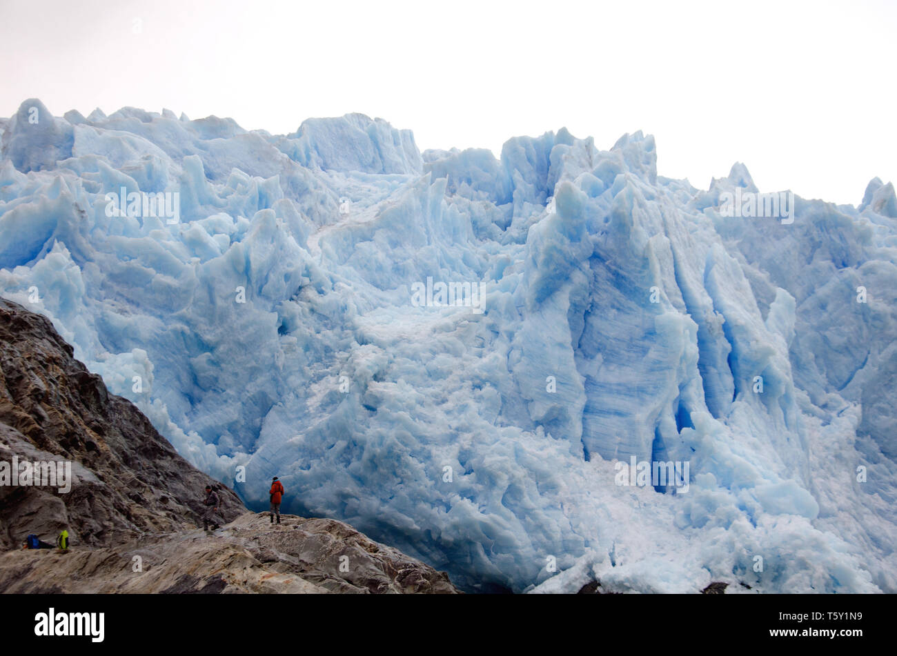 The tiny figures, left, of scientists from an expedition ship, contrast with the steep and lively wall of the El Brujo, or Asia, glacier in a Chile fjord Stock Photo