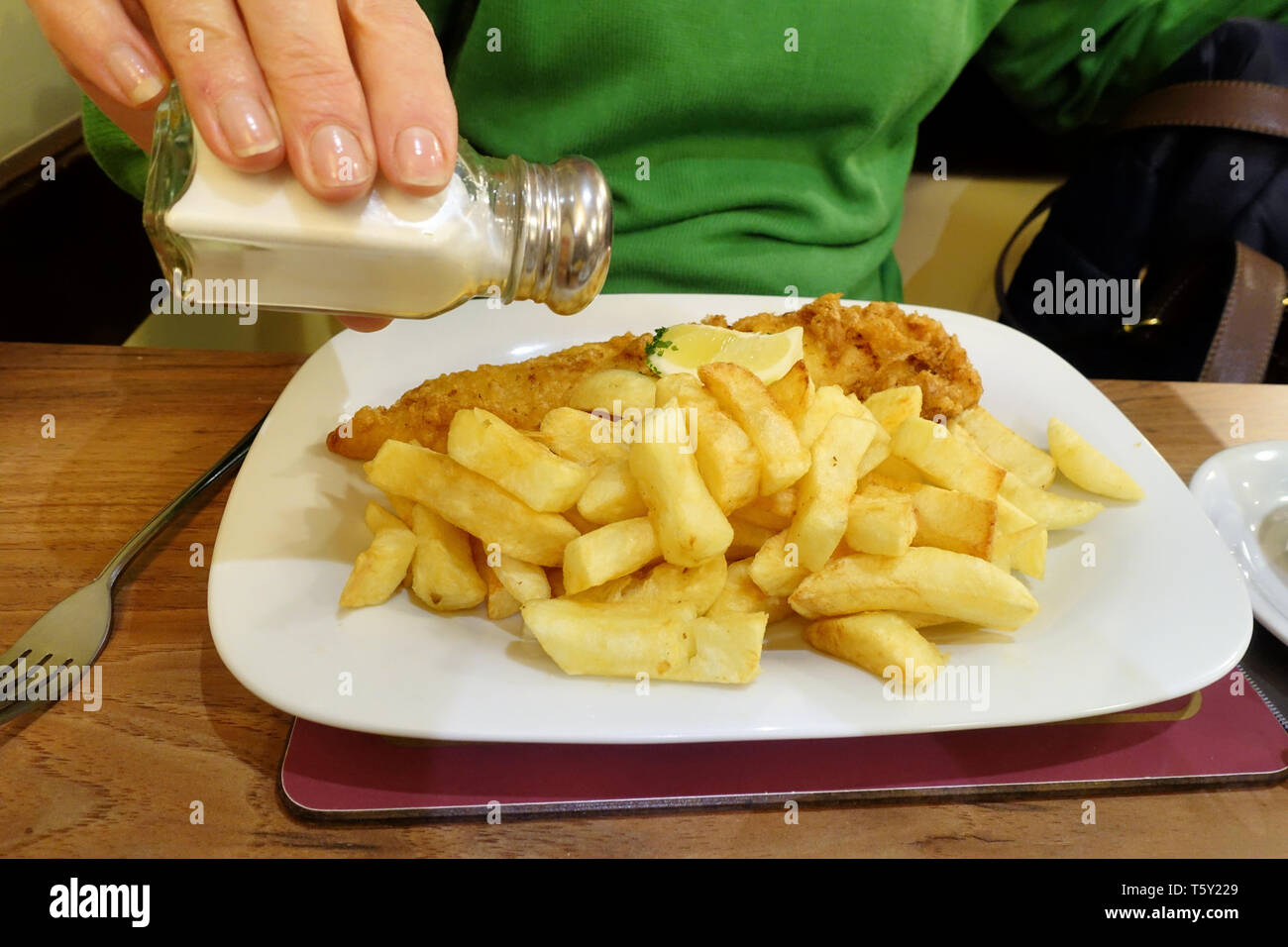 A traditional English Fish and Chip meal served up on a table in a Fish and Chip restaurant. The plates contains fresh battered Cod, chips and tea Stock Photo