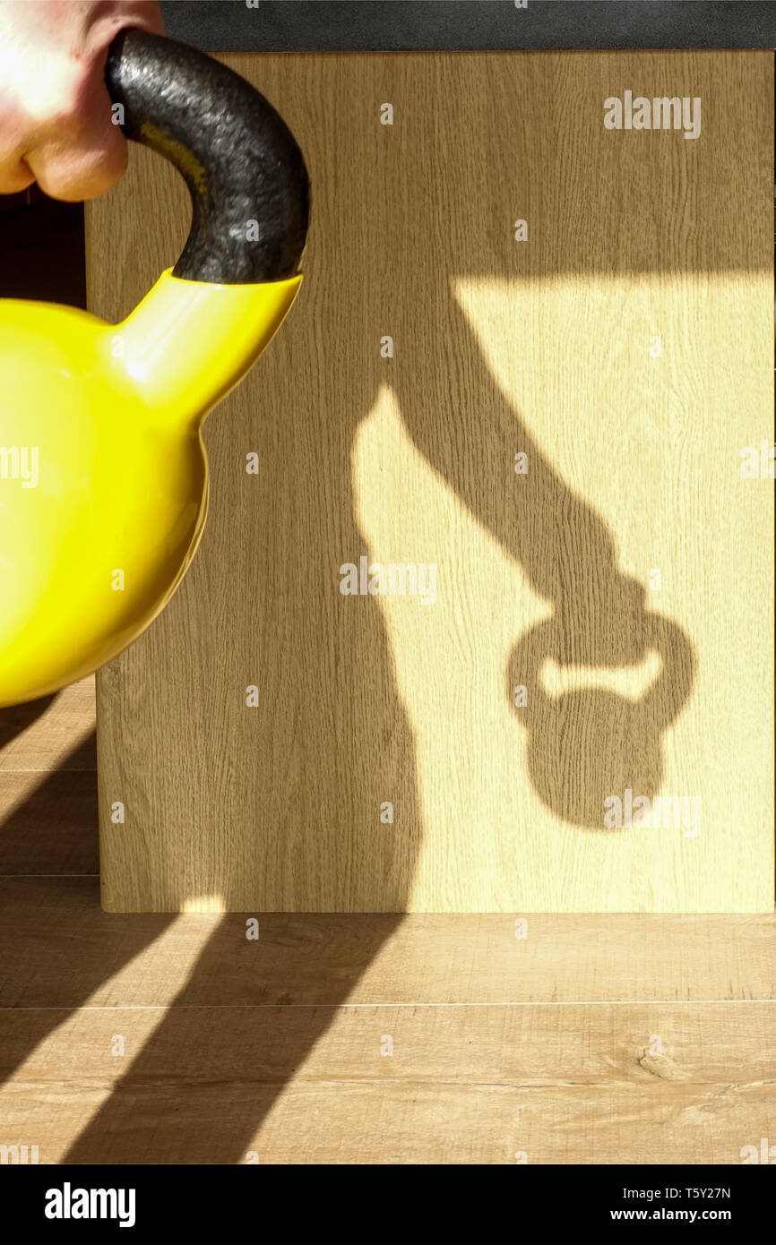 A male working out at home with a kettlebell. The sun is behind him casting a shadow. Kettlebells are a popular home gym option for weight training Stock Photo