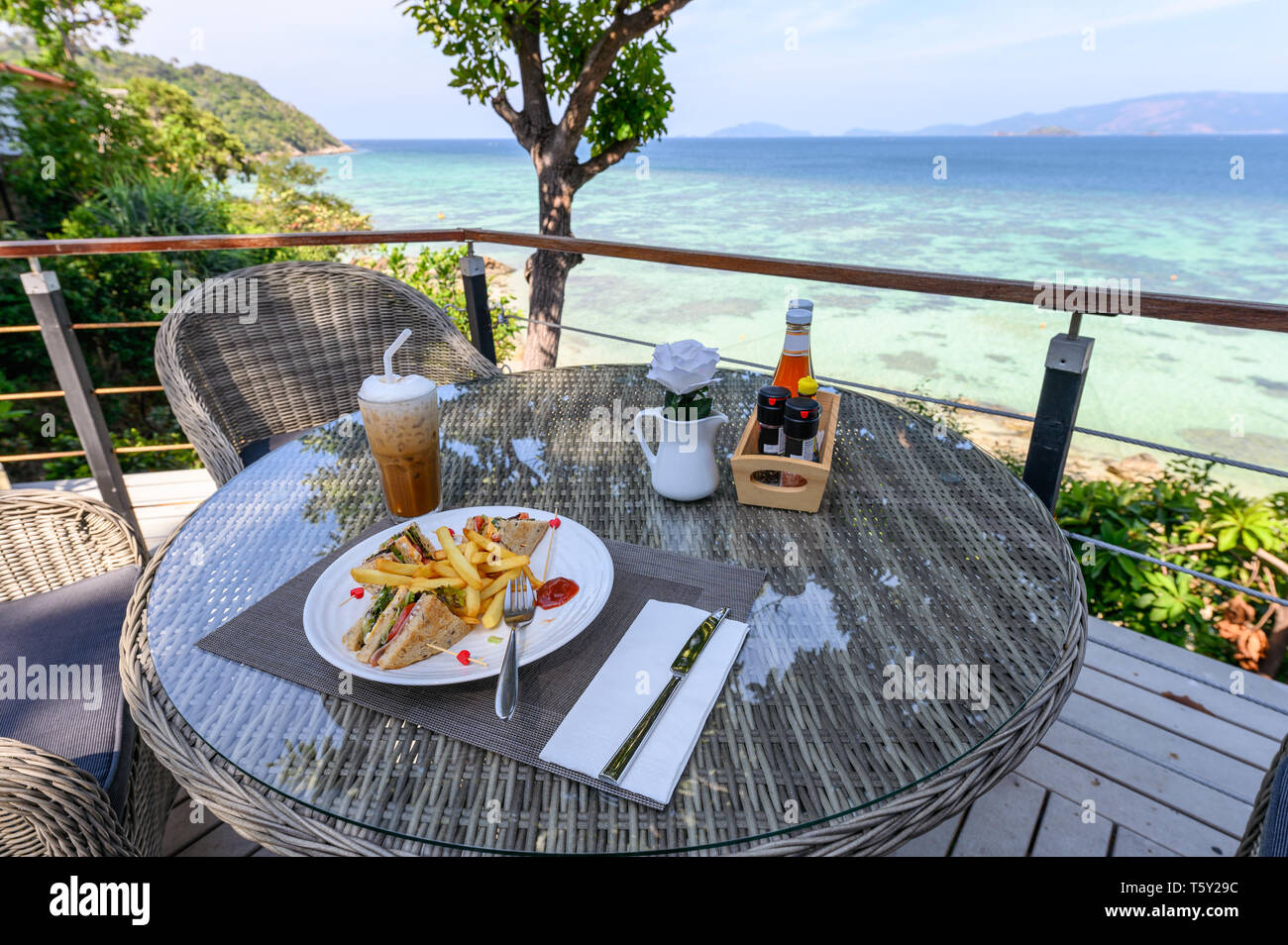 Ham sandwich with vegetables, french-fries and ice coffee on wooden table at patio of sea view in lipe island Stock Photo