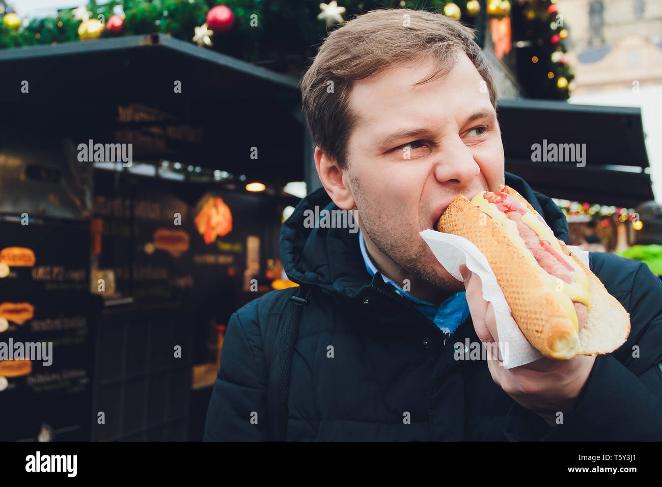 Closeup portrait of hungry man in glasses eating hot dog at outdoors background. Stock Photo