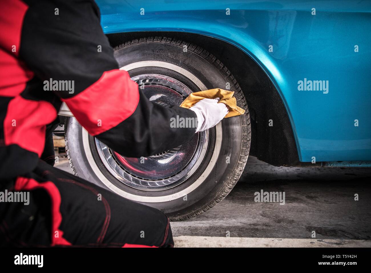 Classic Car Wheels Care. Professional Automotive Worker Cleaning Tire Using Specialized Spray. Stock Photo