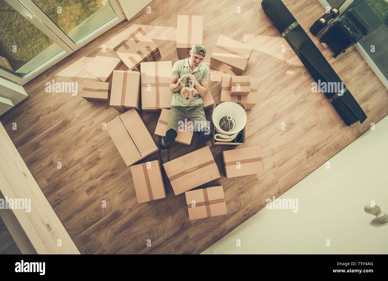Single Men with Dog Moving In. Caucasian Men Between Moving Cardboard Boxes Filled with Personal Stuff and the Australian Silky Terrier in His Hand. H Stock Photo