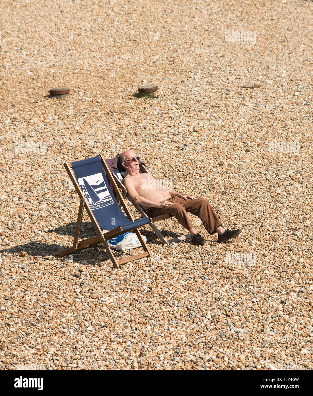 Elderly old male fast asleep whilst sunbathing on a pebble beach in Eastbourne East Sussex England UK Stock Photo
