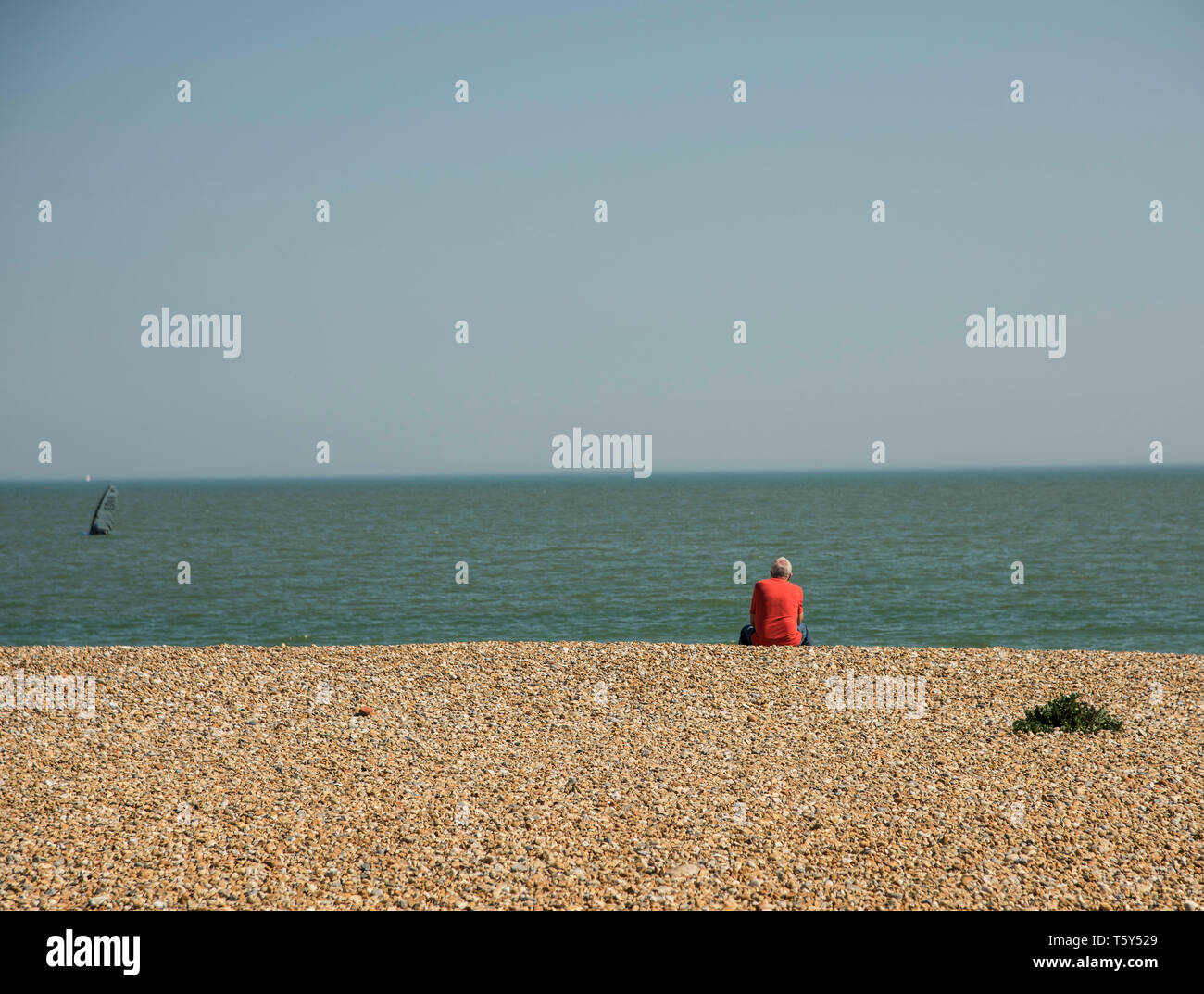 Single Male Wearing A Red Shirt Sitting On The Pebble Beach In single-male-wearing-a-red-shirt-sitting-on-the-pebble-beach-in