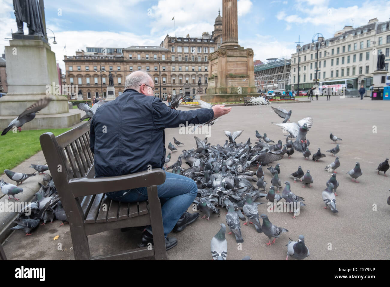 Glasgow, Scotland, UK. 27th April, 2019. UK Weather.  A man sitting on a bench feeding the pigeons on a sunny afternoon in George Square. Credit: Skully/Alamy Live News Stock Photo