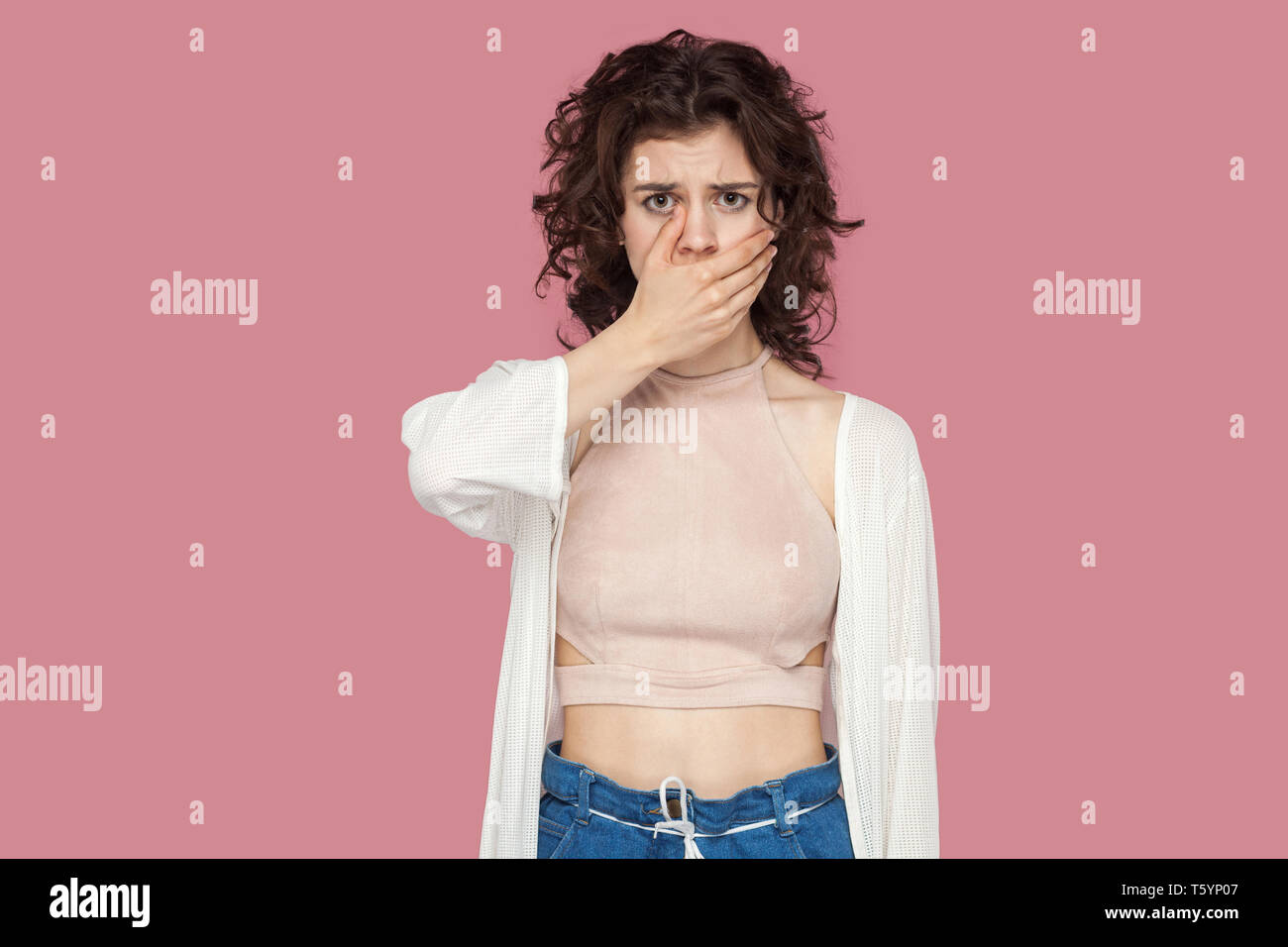 Portrait of shocked worried beautiful brunette young woman with curly hairstyle in casual style standing, covering her mouth and looking at camera. in Stock Photo