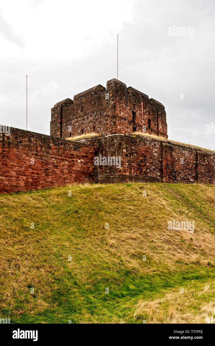 Under a greyish cloudy sky the square four-storey red sandstone keep (or great tower) peers over the curtain wall dominating the castle's skyline Stock Photo
