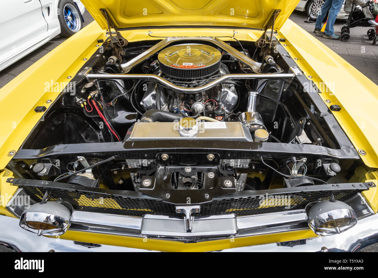 Close-up of the engine of a yellow 1965 Ford Mustang 4700cc car at a classic motor vehicle show in the UK. American automobile with hood open. Stock Photo