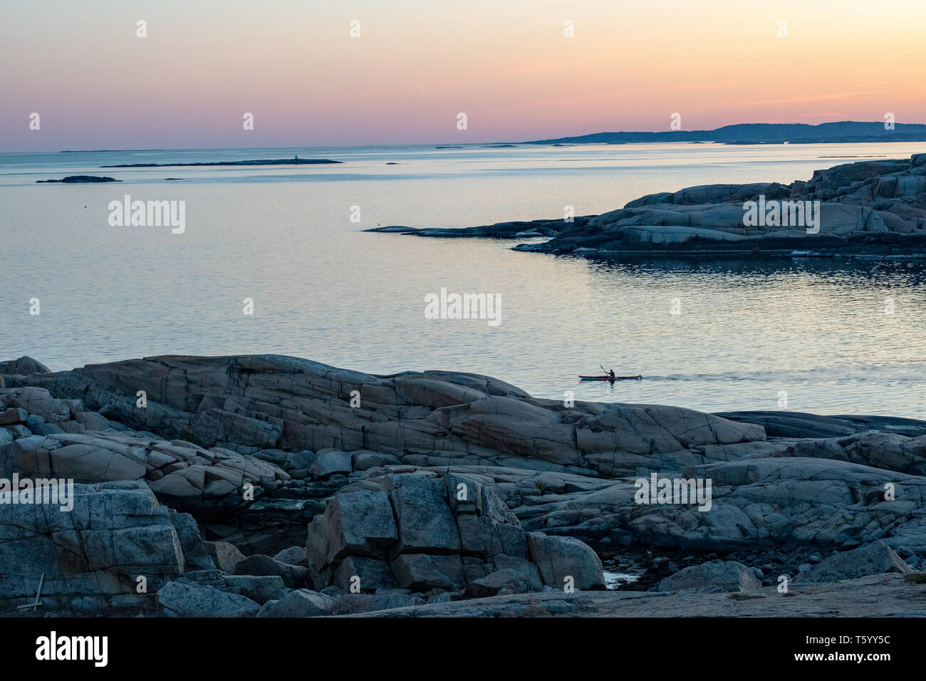 Kayaker on the calm water of 'the end of the world' rocks during sunset in Norway Stock Photo