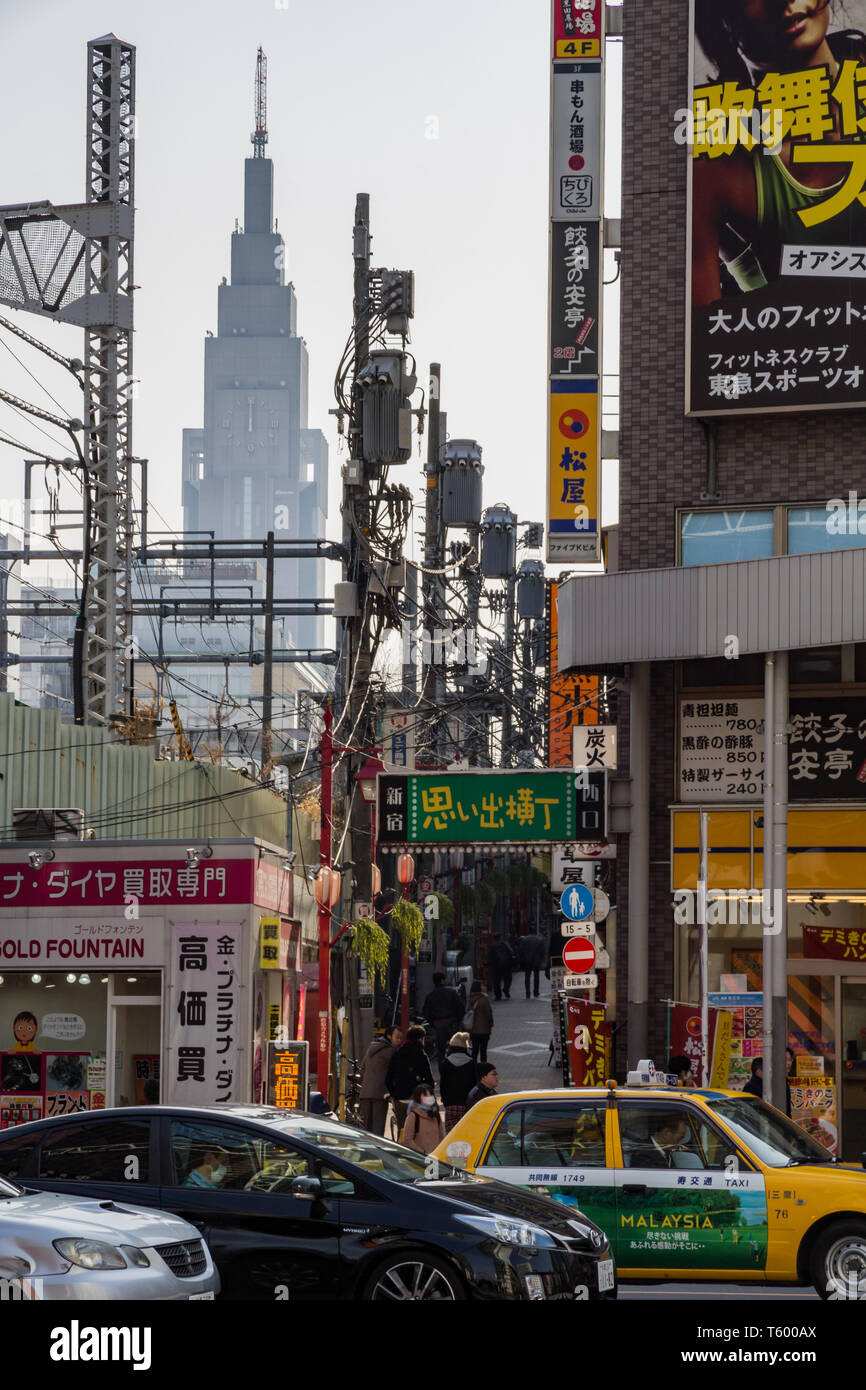 The famous clock tower or NTT Docomo Yoyogi Building appears aligned with the street posts carrying power lines amidst bustling street scene Stock Photo