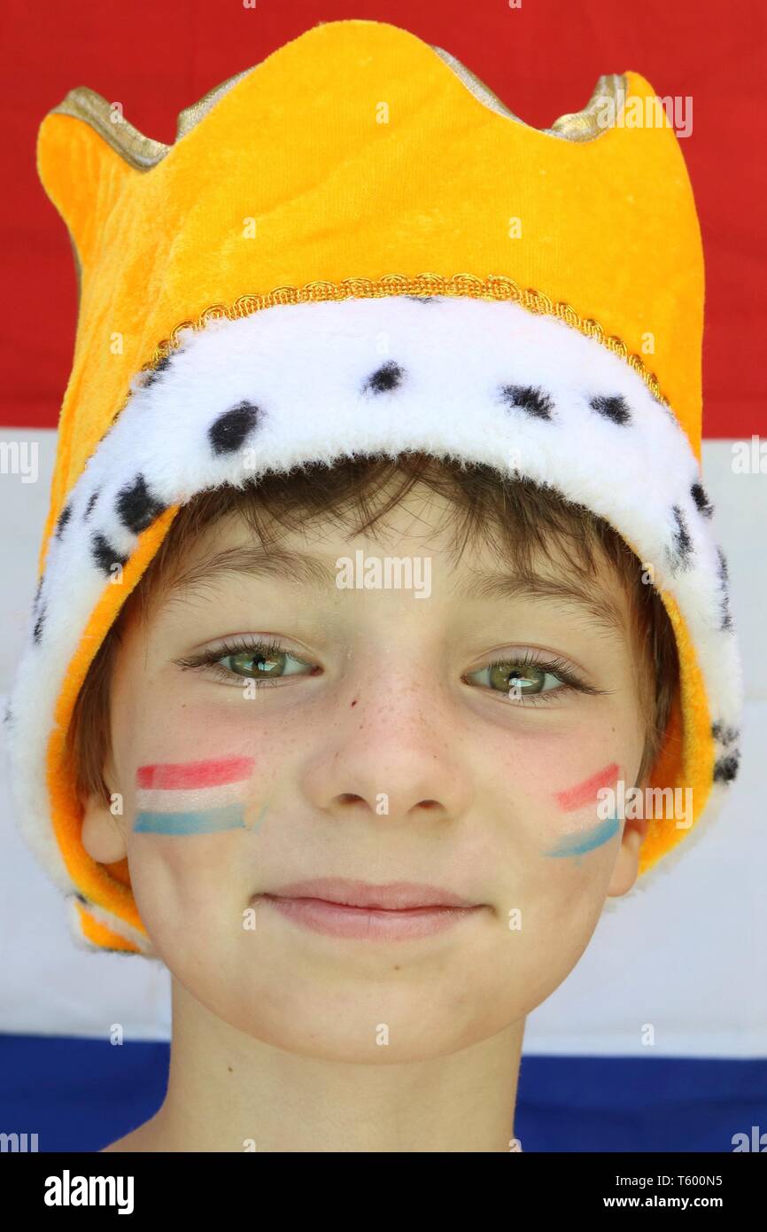Portrait of a child with flags on her cheeks wearing a crown in front of Netherlands flag Stock Photo