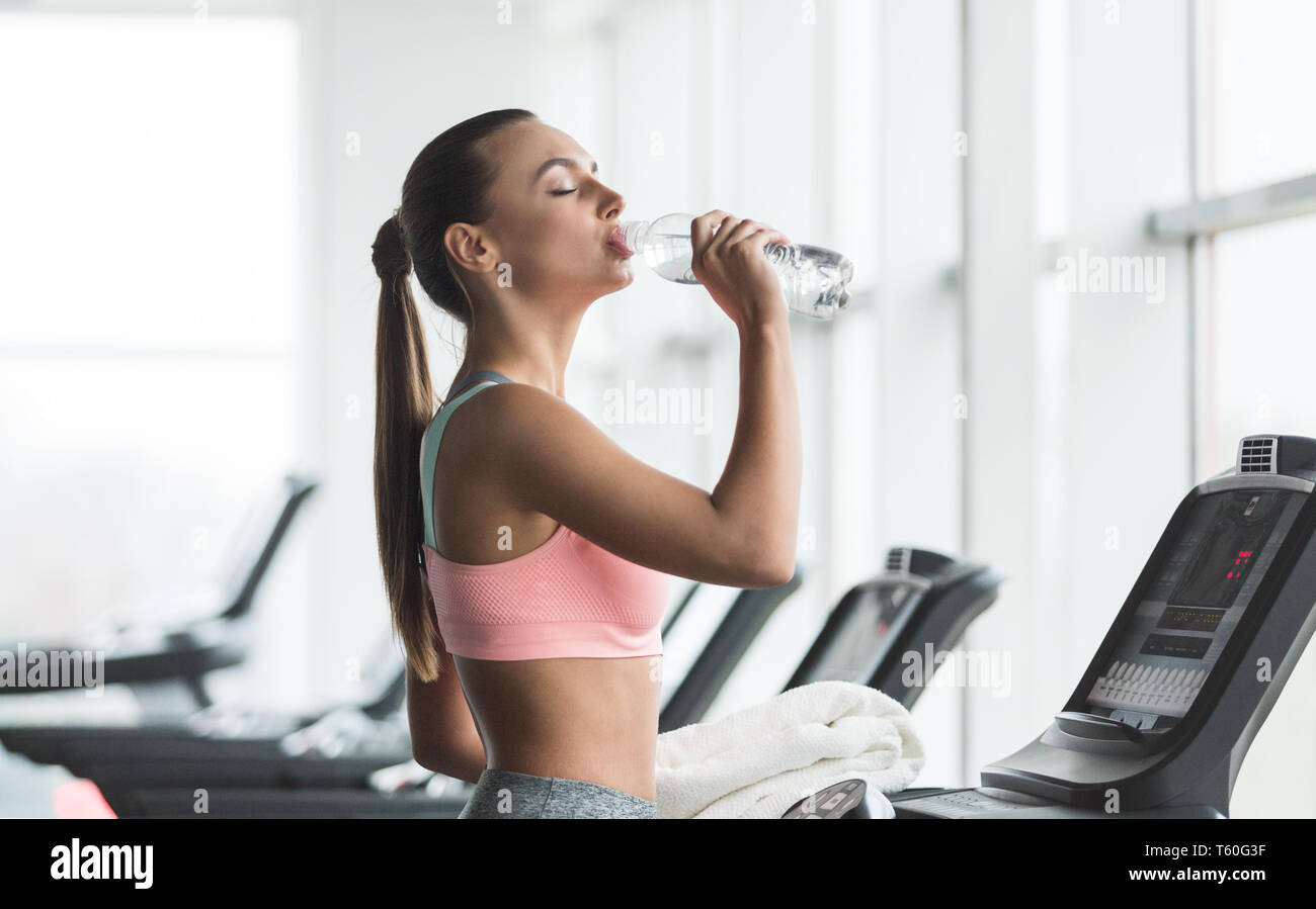 Resting in gym. Woman drinking water after exercising Stock Photo - Alamy, image size:1300x899