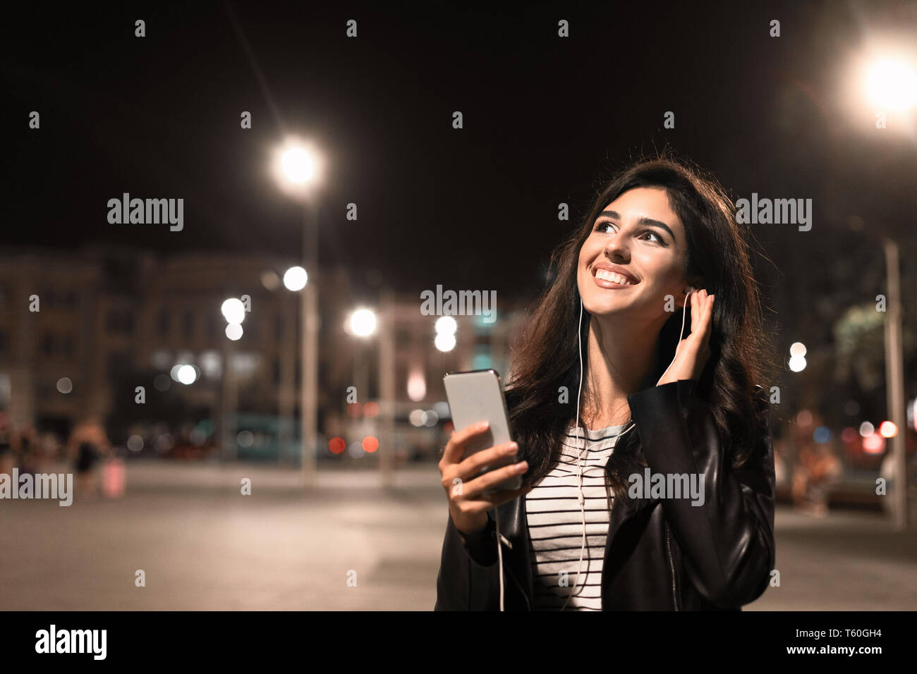 Enjoying walk at night. Girl listening music in earphones in the city Stock Photo