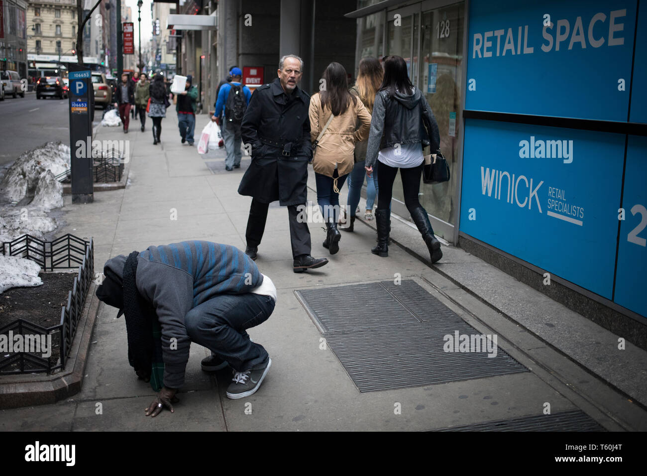 New York City, NY - March 06, 2017: Unidentified Homeless man crouching in the street while other pedestrians  pass by in New York City, NY Stock Photo