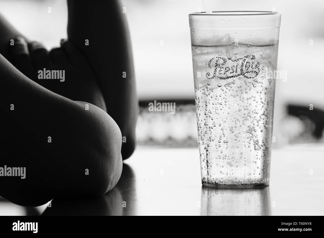 Person sitting at a table in a restaurant with backlit cup of clear soda. Stock Photo