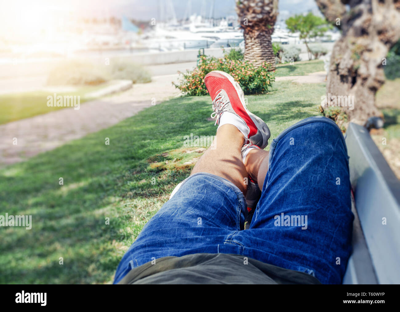 A man in summer clothes and sneakers is lying on a bench in the warm season. Stock Photo