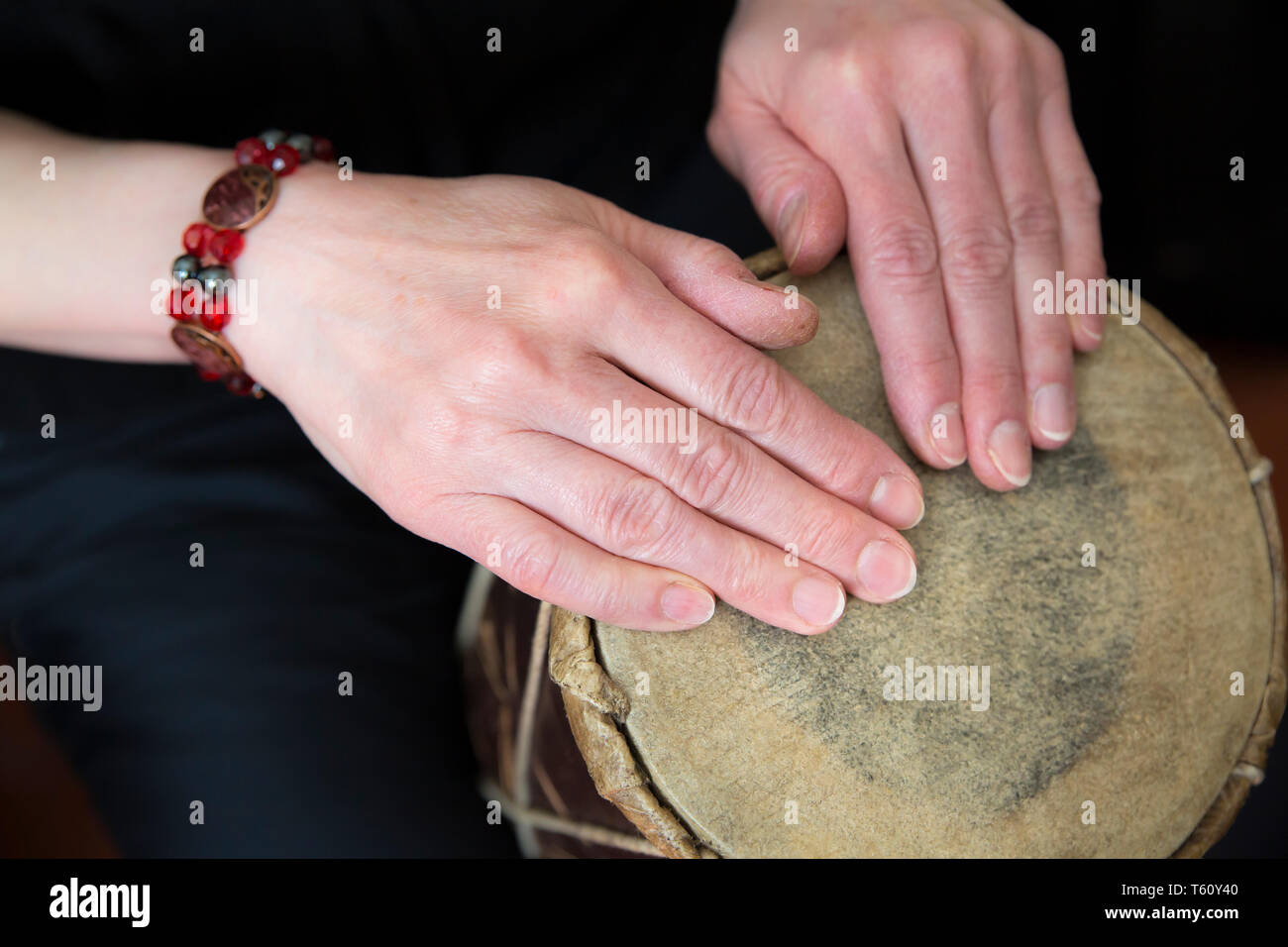 Close up of female hands playing simple, traditional African hand drum (tapping rhythm with finger tips) both hands resting on natural skin drum head. Stock Photo