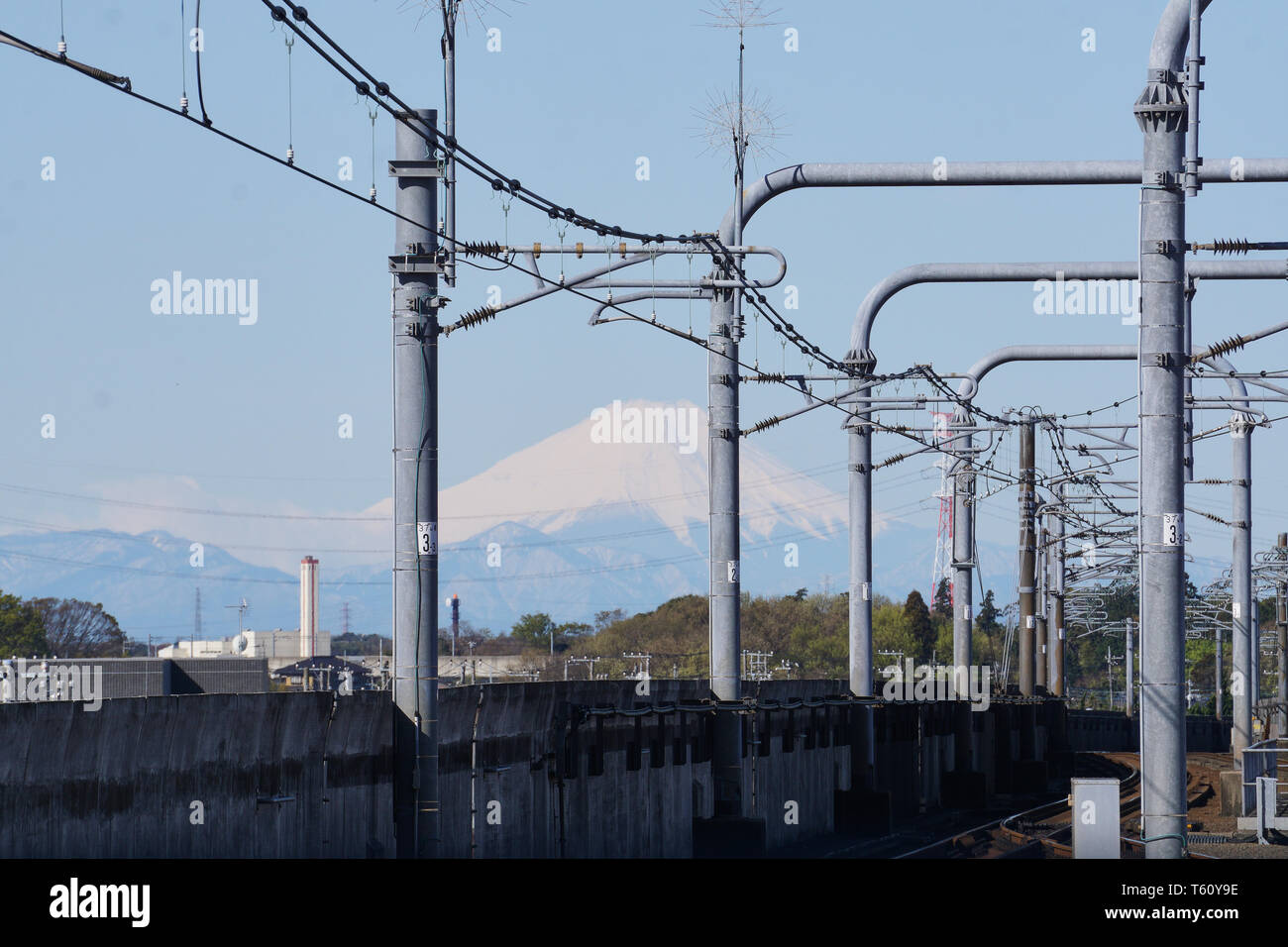 Mount Fuji appears in the distance between power lines and structures built along the tracks on the Tsukuba Express Line from Moriya Station, Ibaraki. Stock Photo