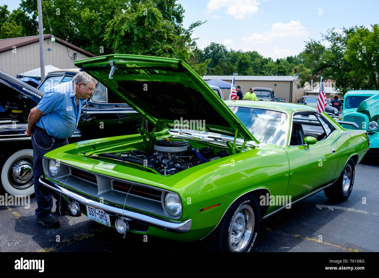White male visitor looking closely at the engine under the hood of a Plymouth Barracuda classic car on an open-air car show in Missouri, USA Stock Photo