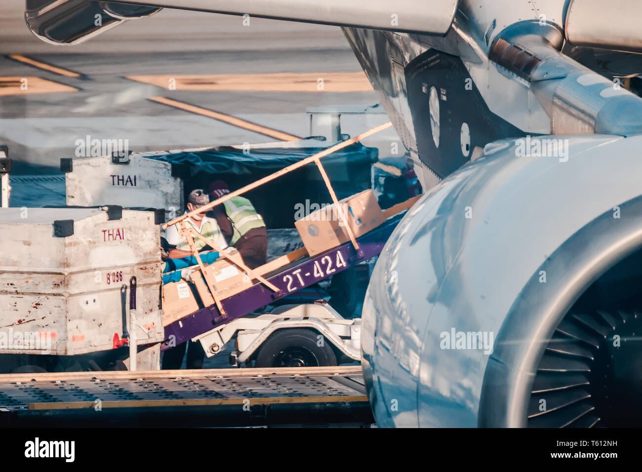 Asian ground crew loading cargo, mail, and luggage including cardboard box into back cargo bay at the airport Stock Photo