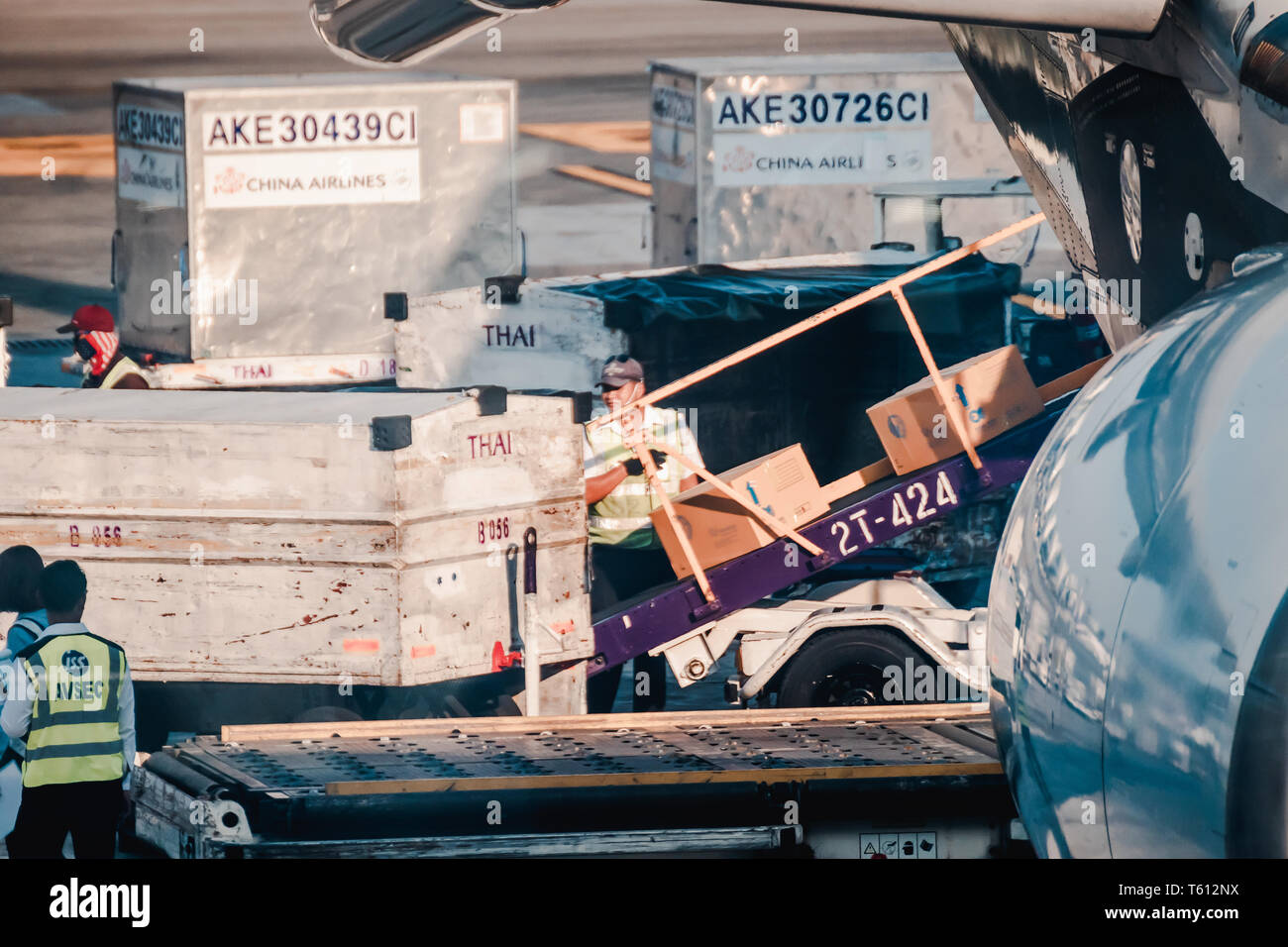 Asian ground crew loading cargo, mail, and luggage including cardboard box into back cargo bay at the airport Stock Photo