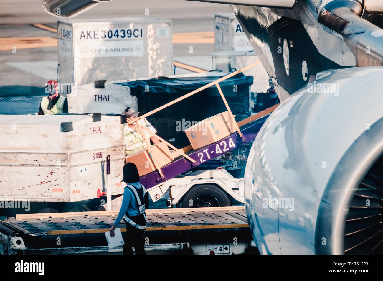 Asian ground crew loading cargo, mail, and luggage including cardboard box into back cargo bay at the airport Stock Photo