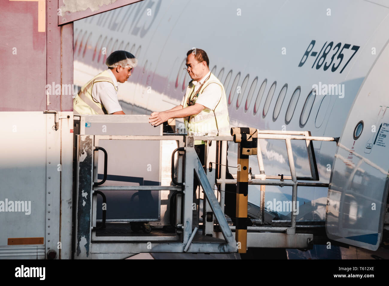 Asian Ground Crew Loading Food And Supply Into A Departing