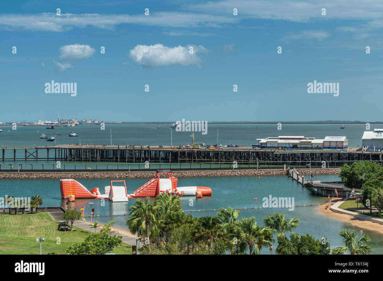 Darwin Australia - February 22, 2019: Big Buoy Water Park with red and white water slide in center of harbour showing boats, warehouses and green zone Stock Photo