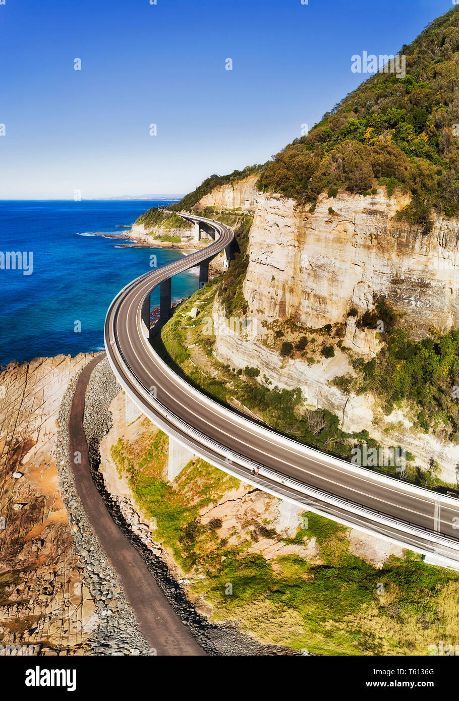 Scenic Grand Pacific drive highway passing Sea Cliff Bridge around steep sandstone cliff on Pacific coast of Australia - aerial vertical view over the Stock Photo