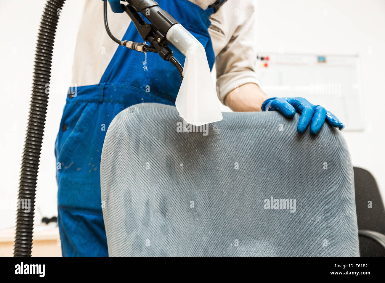Young man in workwear and rubber gloves cleans the office chair with ...
