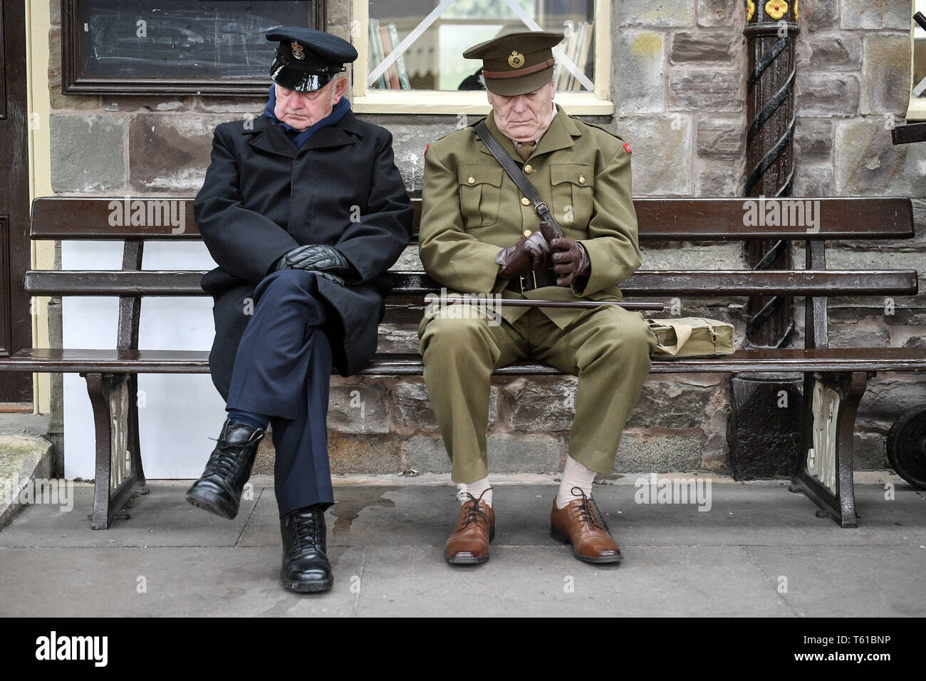 Men dressed in WWII period military uniforms sit on a bench on the platform at Winchcombe during the Wartime in the Cotswolds event at Gloucestershire Warwickshire Steam Railway. Stock Photo