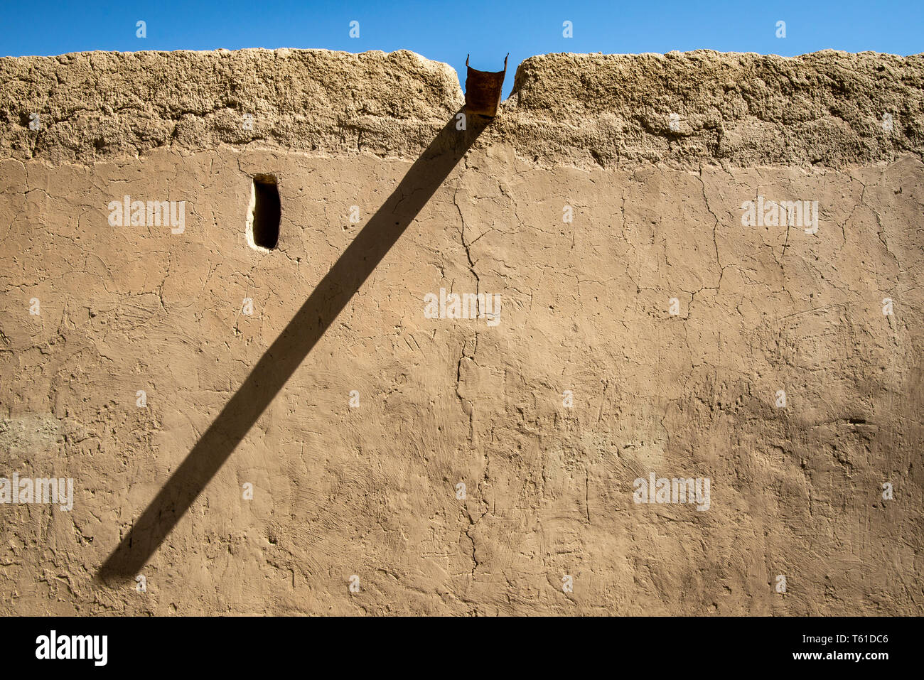Small window and prominent traditional gutter casting a long shadow on the wall of an old renovated Arabian building, Al Ain, United Arab Emirates Stock Photo