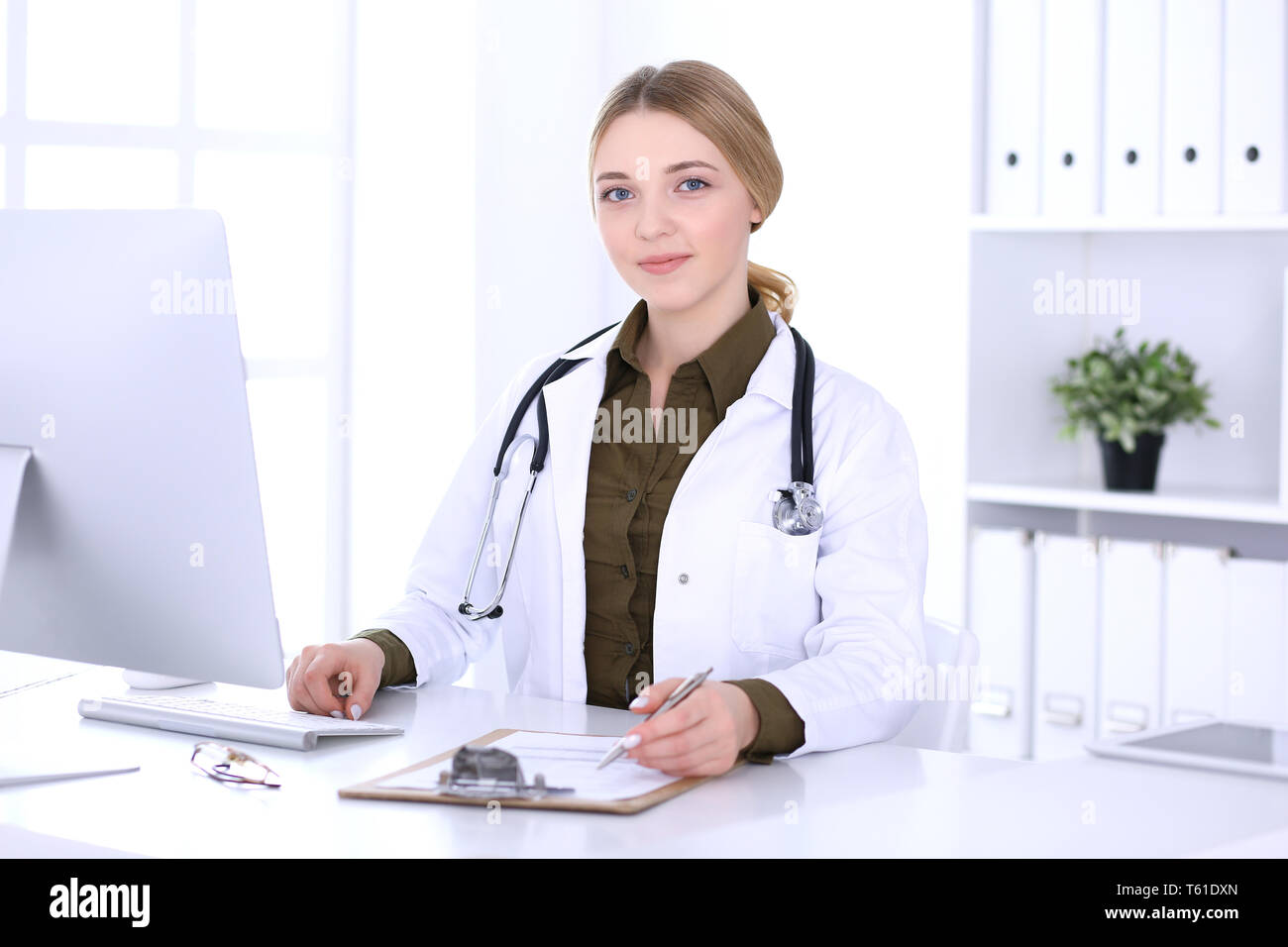 Young woman doctor at work in hospital looking at desktop pc monitor. Physician controls medication history records and exam results. Medicine and Stock Photo