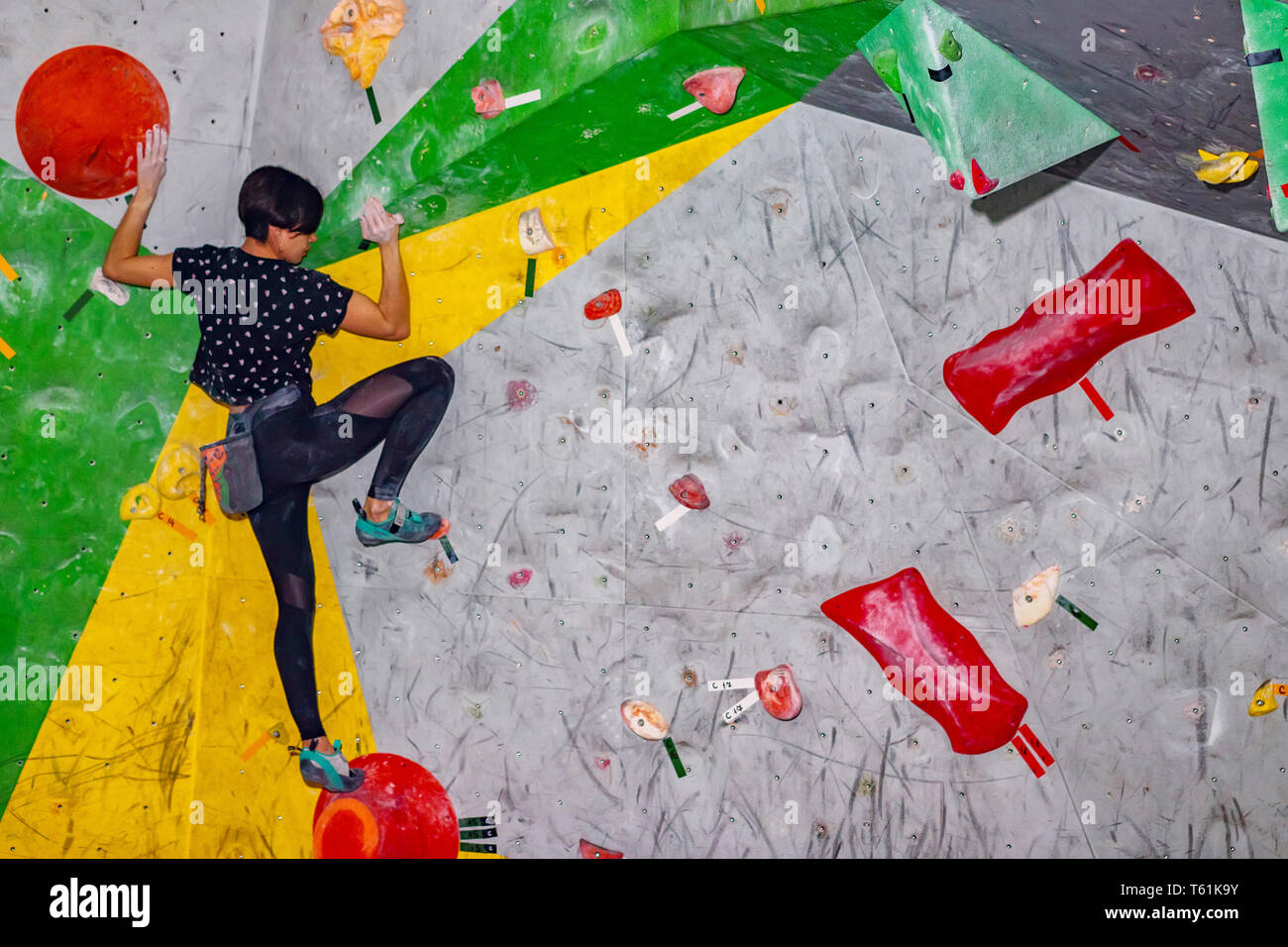 Rock climber woman hanging on a bouldering climbing wall, inside on