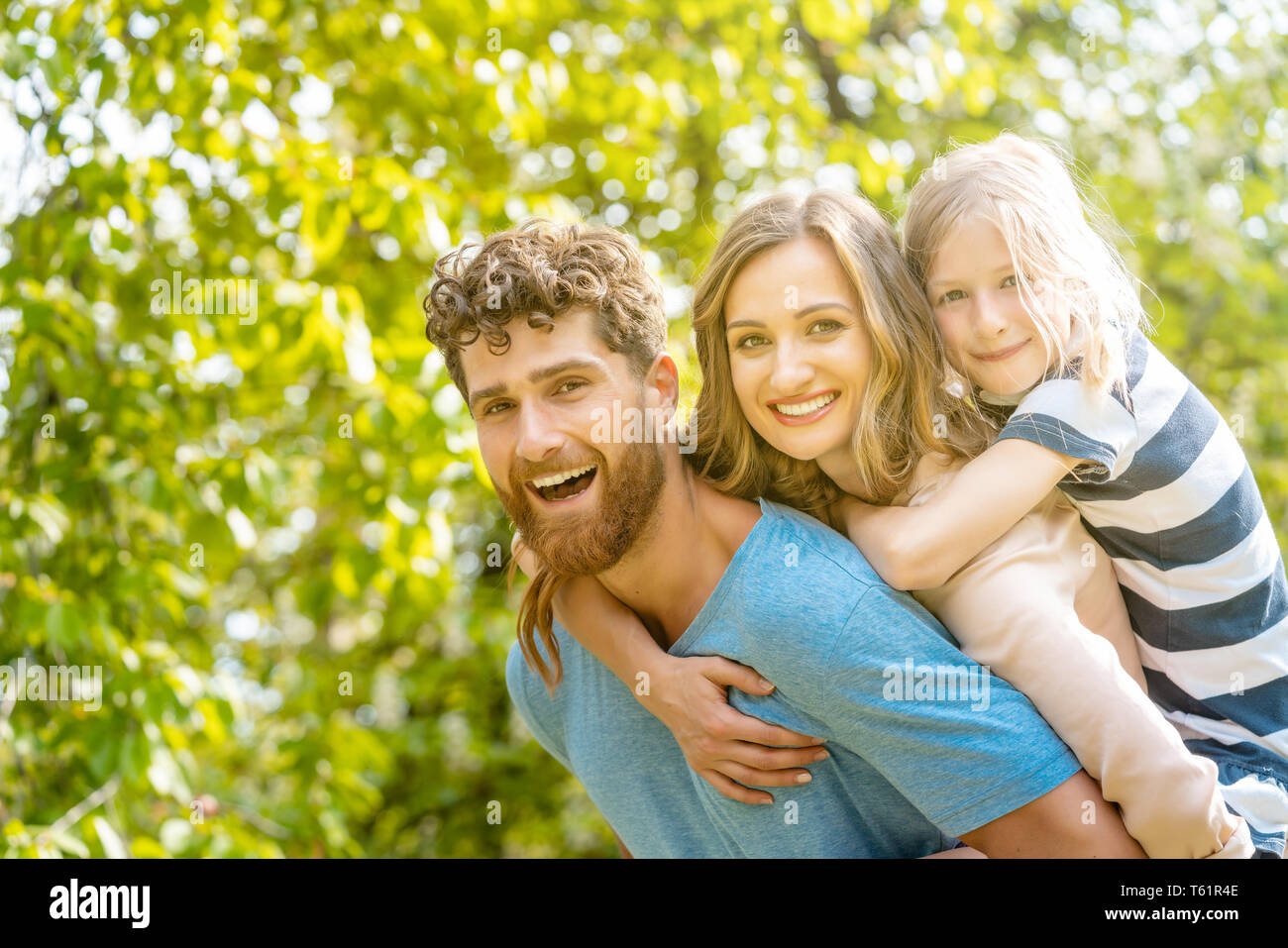 Strong man supporting his family by carrying wife and daughter piggyback Stock Photo