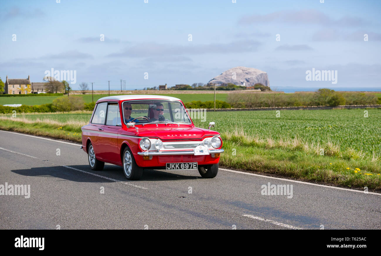 East Lothian, UK. 28 April 2019. Classic Car Tour: North Berwick Rotary Club holds its 3rd rally with 65 classic cars entered. The car rally route is from East Lothian and back through the Scottish Borders, raising money for local charities. A red 1967 875cc Hillman Imp driving past Bass Rock on the Firth of Forth coast Stock Photo