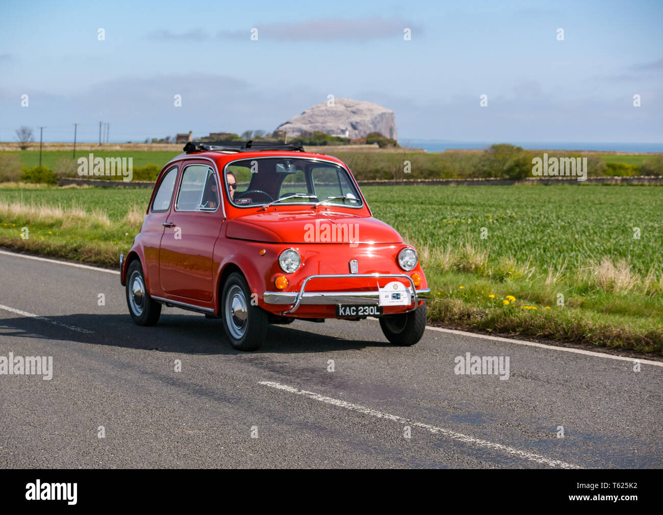 East Lothian, UK. 28 April 2019. Classic Car Tour: North Berwick Rotary Club holds its 3rd rally with 65 classic cars entered. The car rally route is from East Lothian and back through the Scottish Borders, raising money for local charities. A vintage 1972 orange Fiat 500 with Bass Rock gannet colony on a Scottish country road Stock Photo