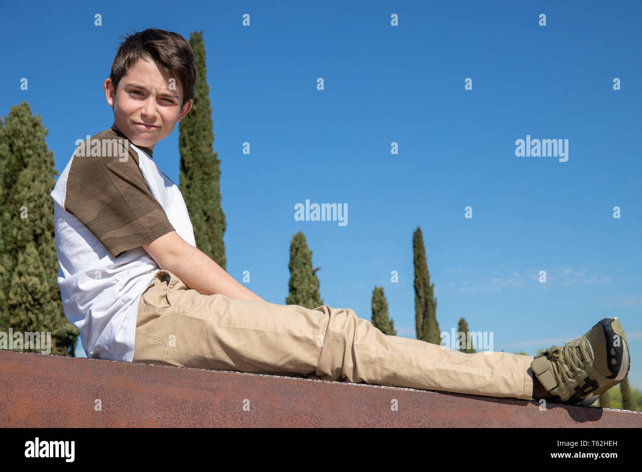 Thirteen-year-old boy sitting on a fence with blue sky in the background Stock Photo