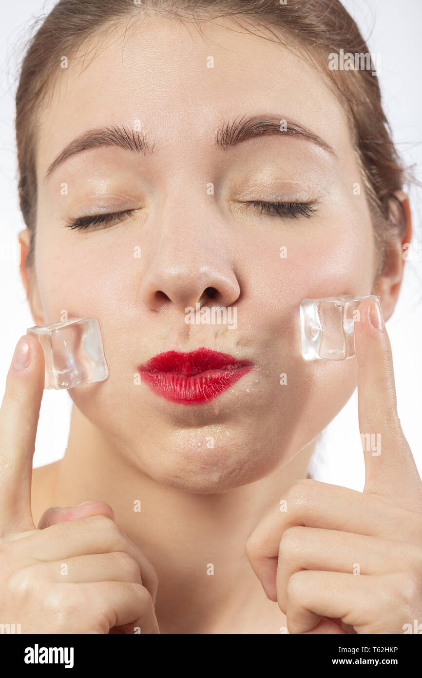 serious young woman applying ice cubes on her face skin, isolated on