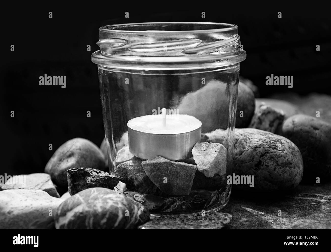 black and white tea light candle glass stones center dark background by