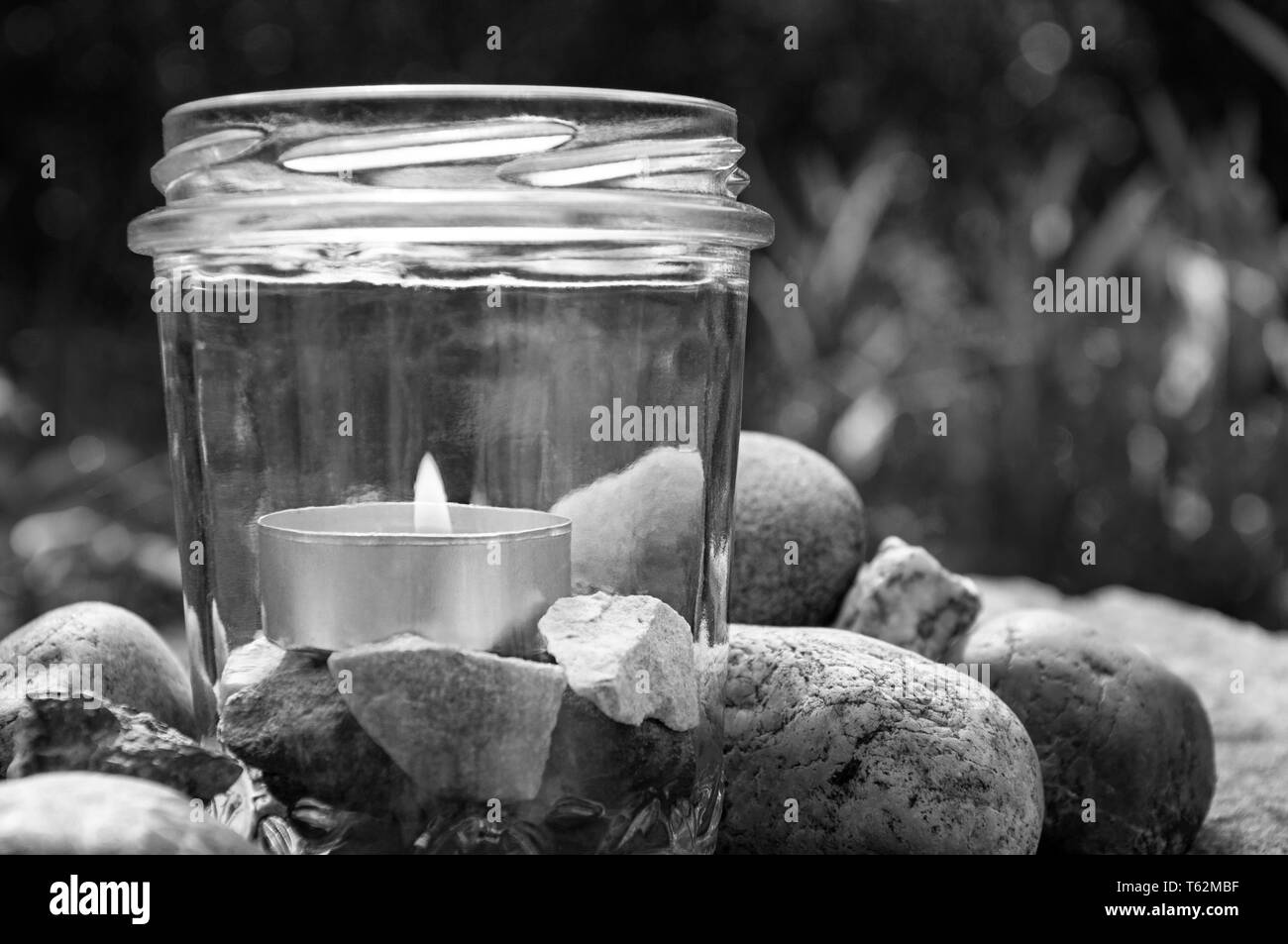 black and white burning tea light candle glass stones left grasses background  by jziprian Stock Photo