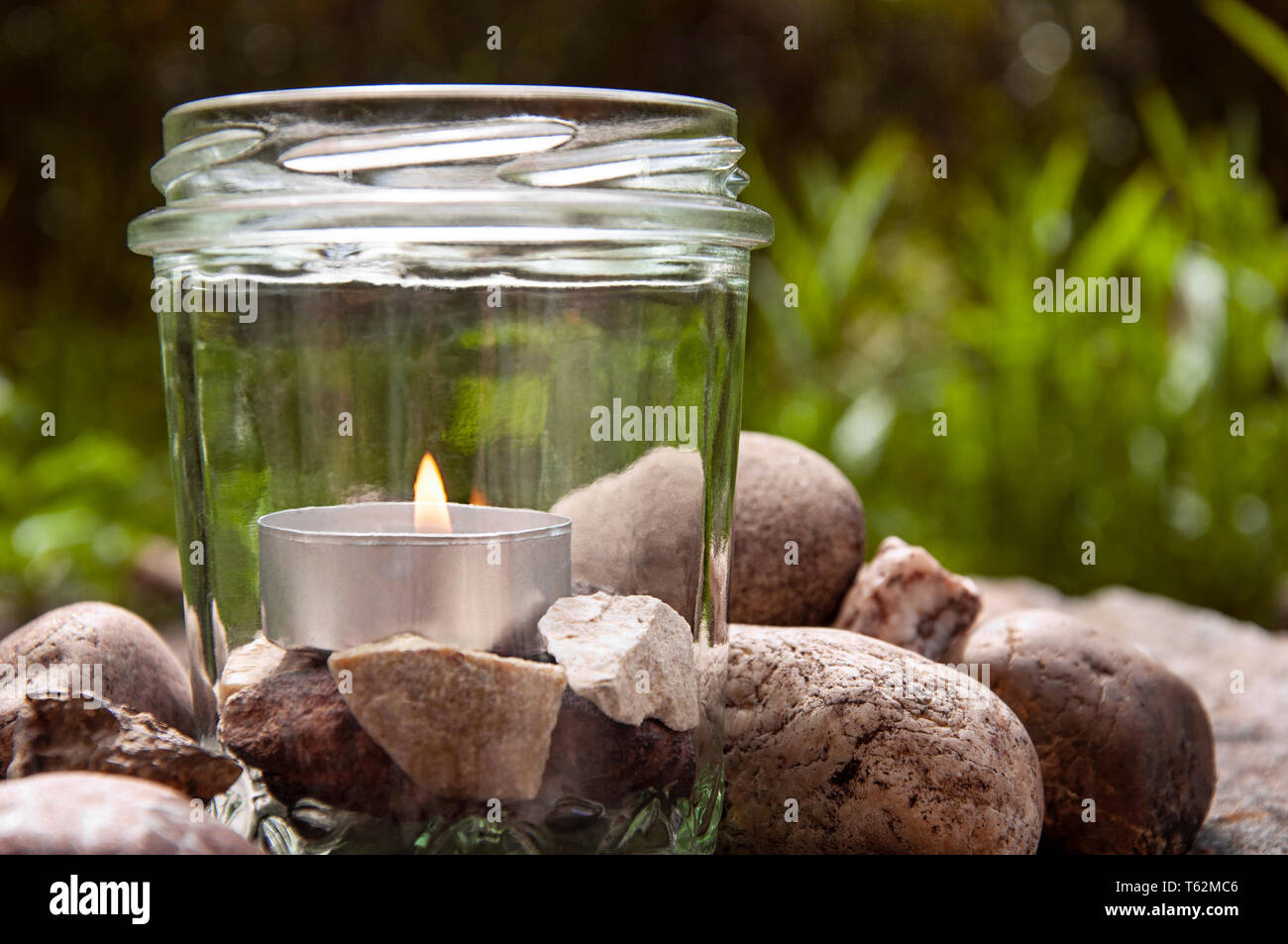 Burning tea light candle glass stones left grasses background by