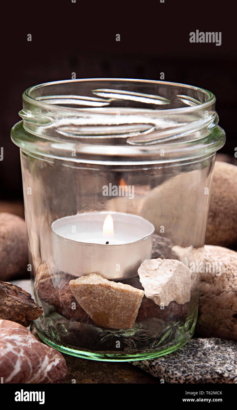 upright white burning tea light candle glass stones center dark